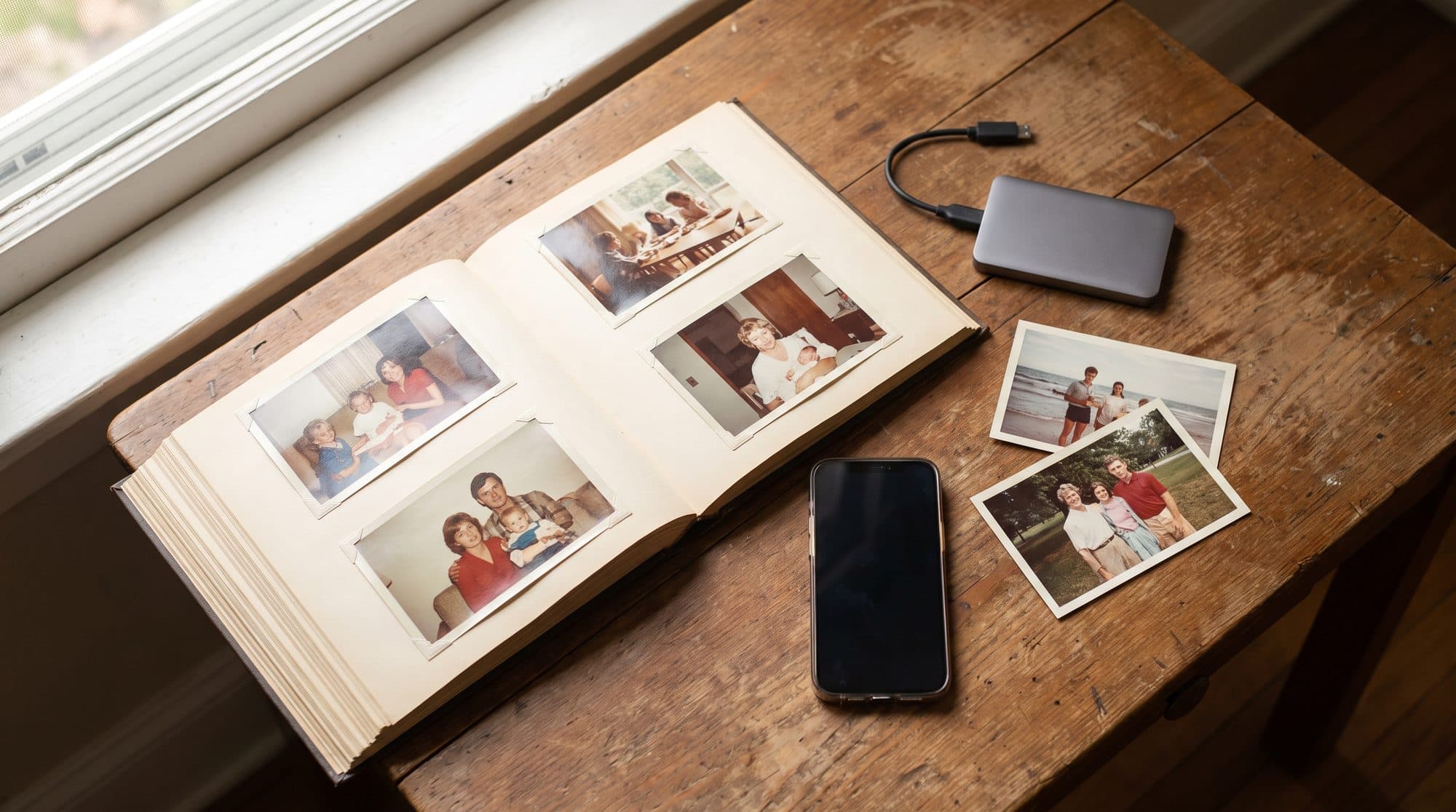 Čuvanje uspomena: otvoren foto album sa porodičnim slikama, pametni telefon i eksterni SSD disk